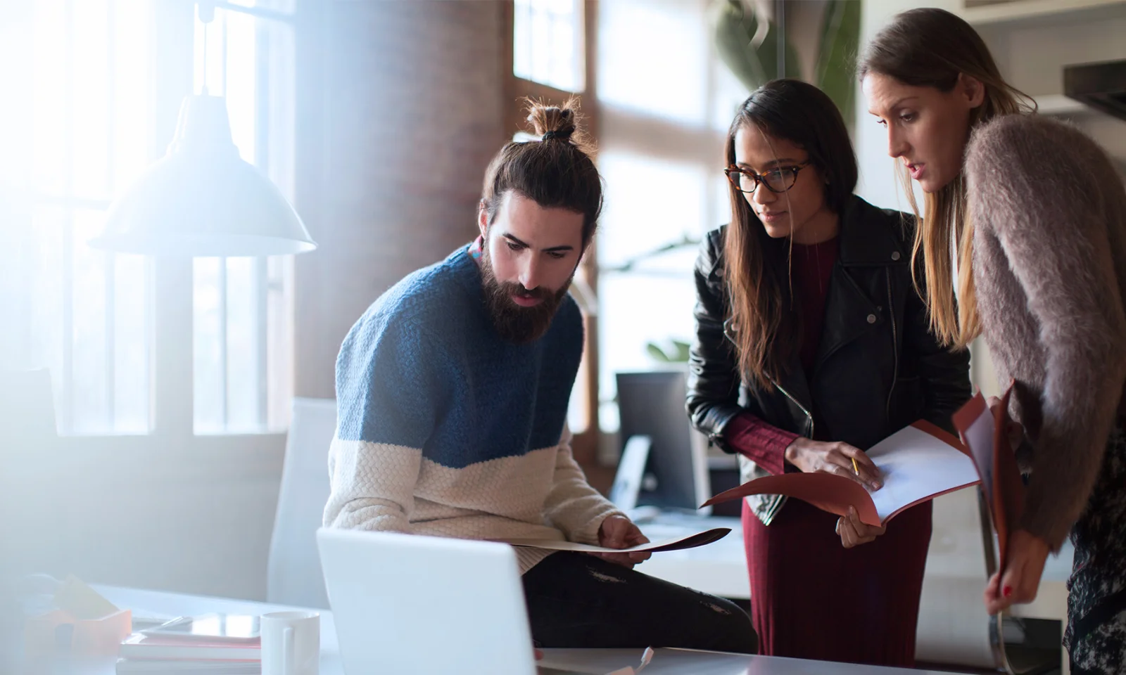 GFT and 10x Banking Collaboration – Driving Financial Innovation Three professionals collaborating around a laptop, symbolising the partnership between GFT and 10x Banking to drive innovation in the financial services sector.
