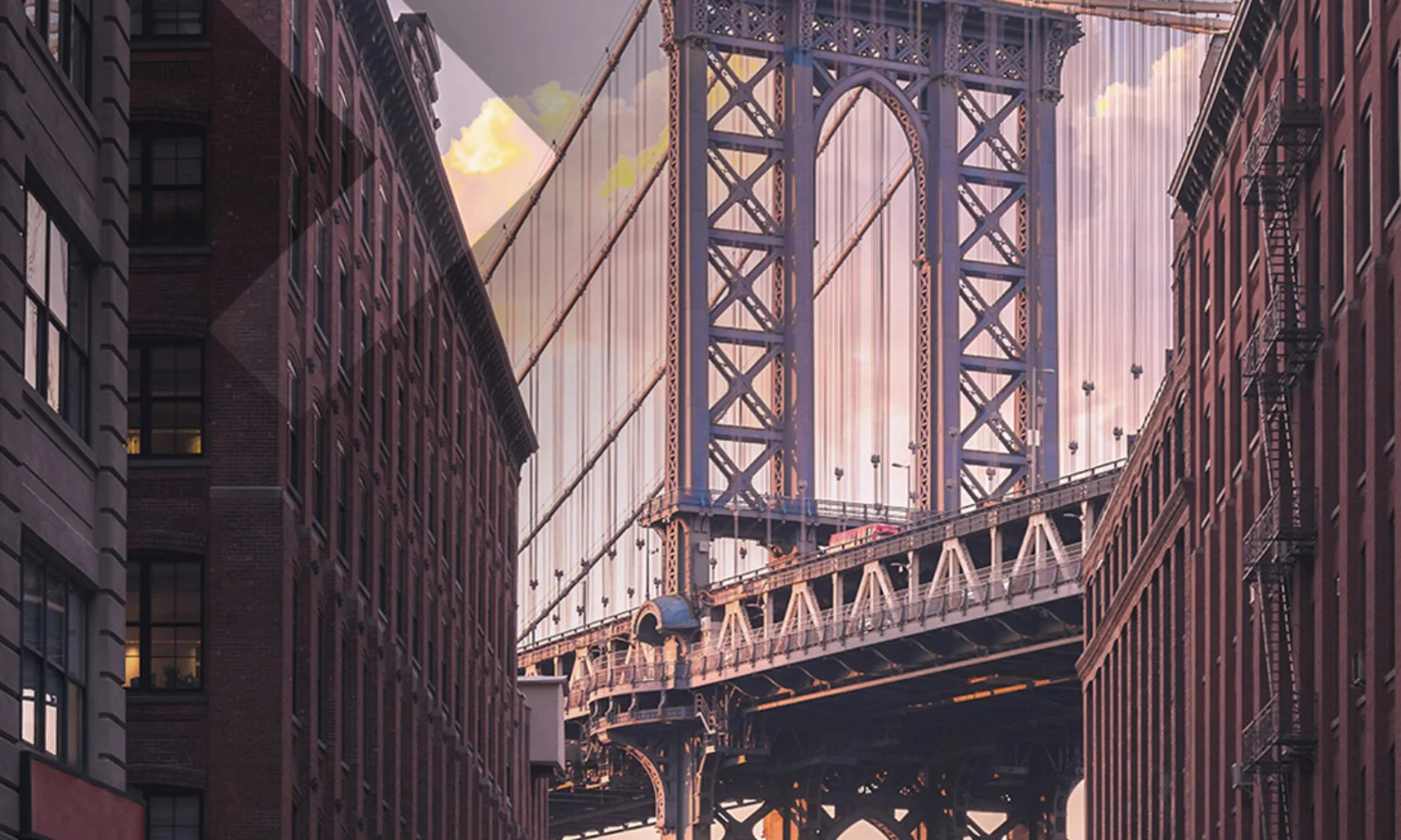 What is Open Banking - 00 A view of the Manhattan Bridge framed by tall urban buildings at sunset, showcasing the architectural beauty and urban landscape of New York City.