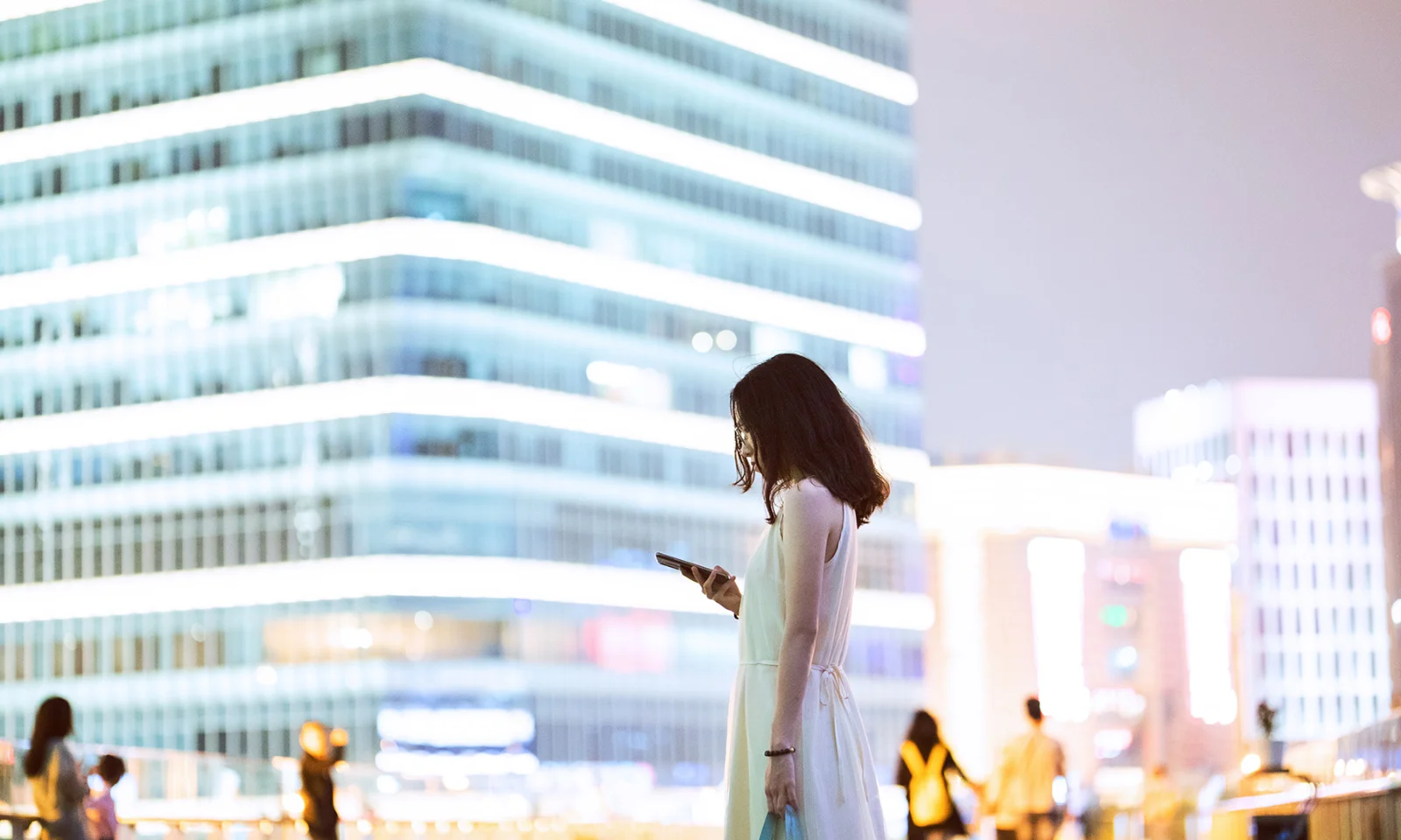 Explore las percepciones erróneas comunes sobre la digitalización bancaria con esta impactante imagen. Descubra cómo la transformación digital en el sector bancario está transformando las experiencias de los clientes, mejorando la seguridad e impulsando la innovación. Conozca los mitos y las realidades de la adopción de soluciones digitales en la industria financiera y comprenda el verdadero potencial de la digitalización tanto para los bancos como para sus clientes. Descubra los hechos detrás de la digitalización bancaria y su papel en el futuro de las finanzas. Una mujer parada en un entorno urbano por la noche, mirando su teléfono inteligente, con edificios modernos brillantemente iluminados en el fondo, que representan el tema de la digitalización en la banca.