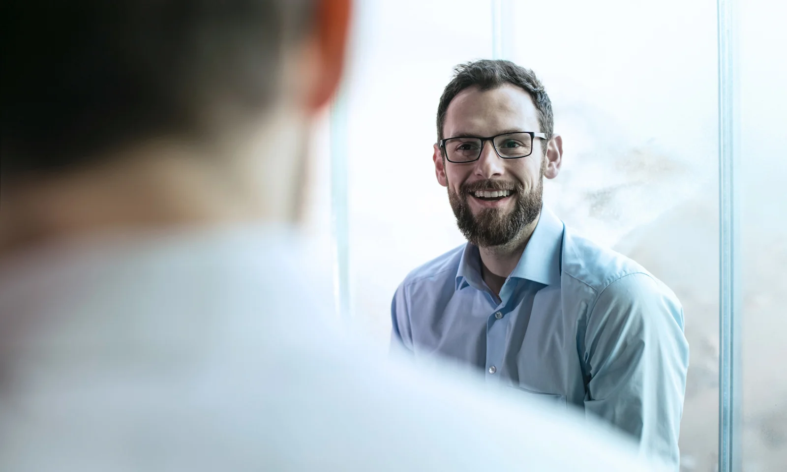 Rulex-Schlüsselvisual Ein Key Visual für Rulex, das einen Geschäftsmann mit Brille zeigt, der während eines Gesprächs in einem hellen Büro lächelt. Dieses Bild unterstreicht den Fokus von Rulex auf benutzerfreundliche, fortschrittliche Analyse- und Entscheidungsautomatisierungslösungen. Entdecken Sie, wie die innovativen Technologien von Rulex in Zusammenarbeit mit GFT Ihr Unternehmen mit datengesteuerten Erkenntnissen und Automatisierung stärken können.